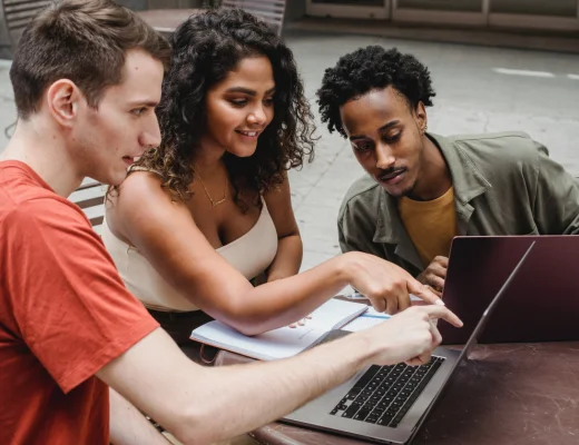 Drei junge Menschen sitzen um einen Tisch vor einem Laptop
