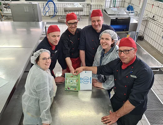 Eine Gruppe von Personen steht in einer Großküche um einen Tisch