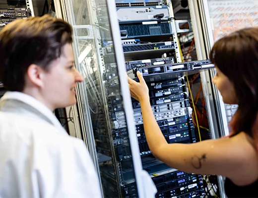 Zwei Frauen stehen vor einer Serveranlage mit dem Rücken, ein nimmt eine Festplatte raus