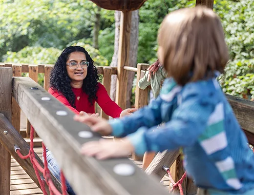Eine junge Frau auf einem Klettergerüst mit ausgestreckten Armen zu zwei Kindern