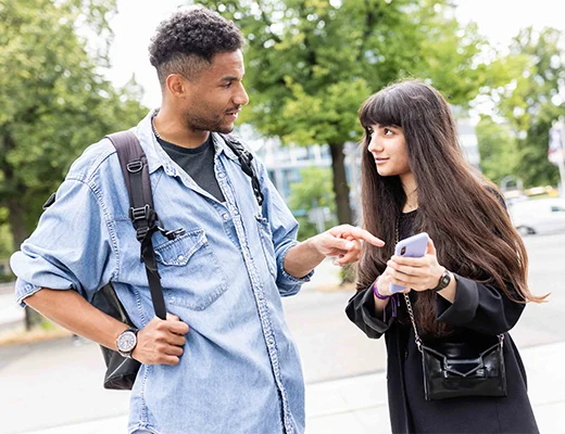 Ein junger Mann und eine junge Frau unterhalten sich, sie hat ihr Handy in der Hand und zeigt drauf