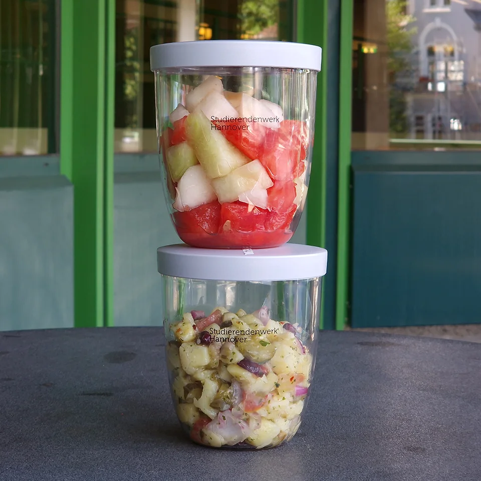 Zwei transparente Mehrwegcups mit Essen befüllt auf einem Tisch