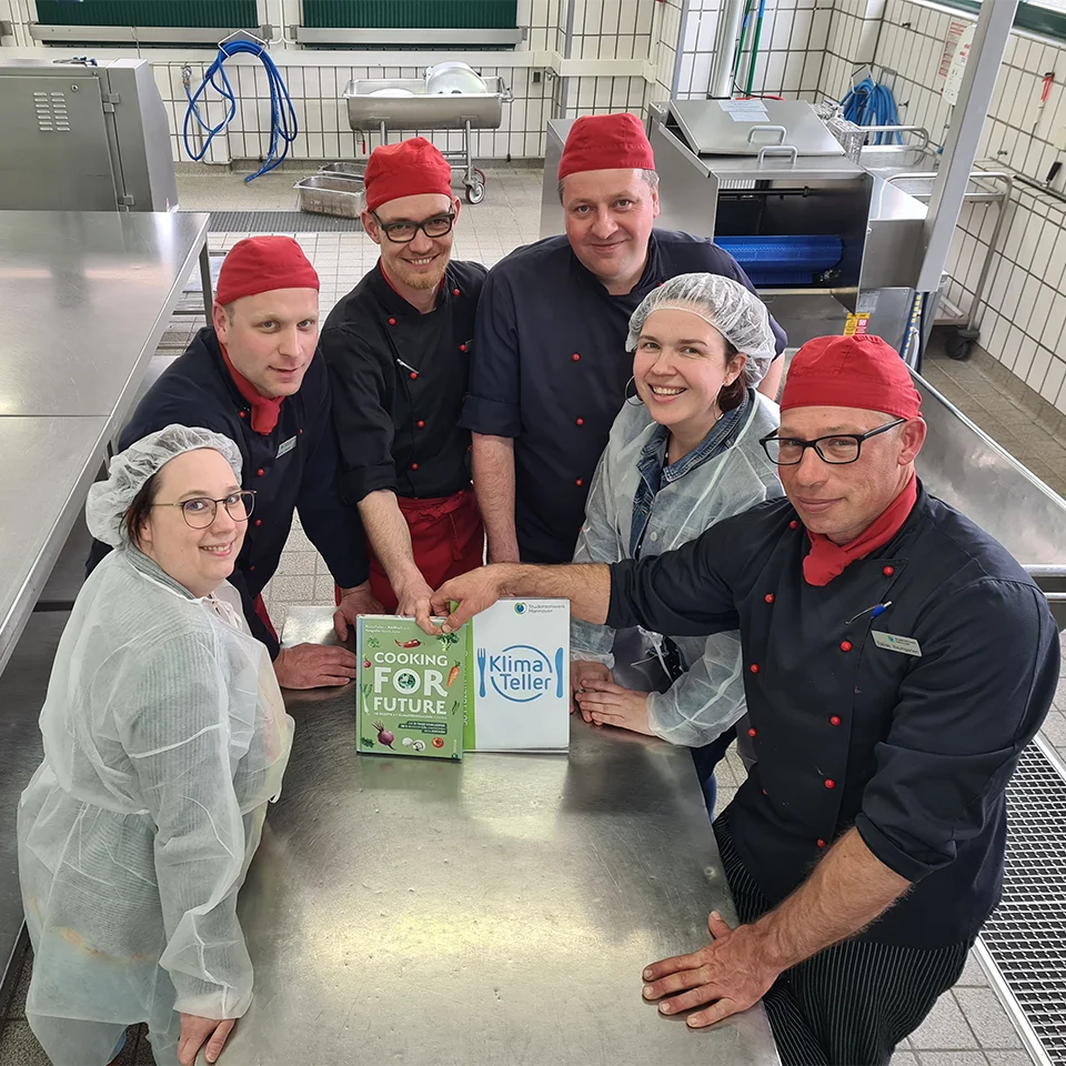Eine Gruppe von Personen steht in einer Großküche um einen Tisch