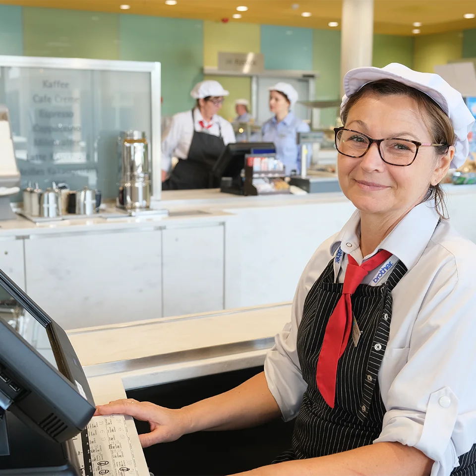 Eine Frau sitzt an der Kasse und lächelt in die Kamera