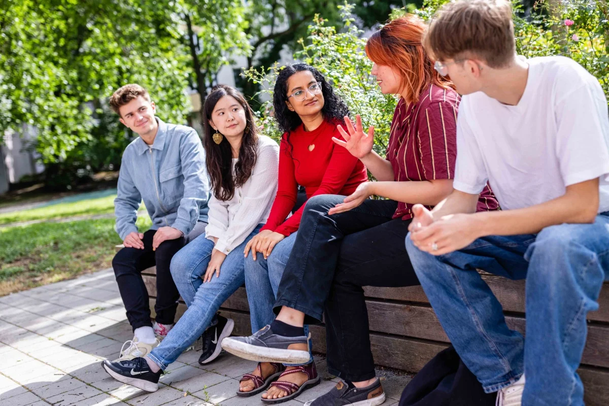 Fünf junge Menschen sitzen draußen auf einer Bank und unterhalten sich